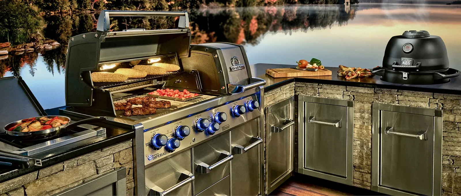 Broil King Imperial beépített gázgrill és KEG kamado kőborítású kültéri konyhában, tóparti naplementében